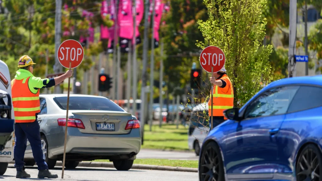 Two traffic controllers hold STOP signs to control vehicles at a road intersection