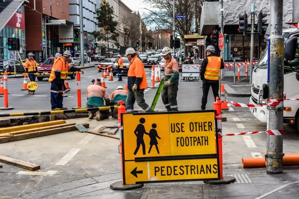 Road crew at a city footpath excavation beside a "Use other footpath" pedestrian detour sign