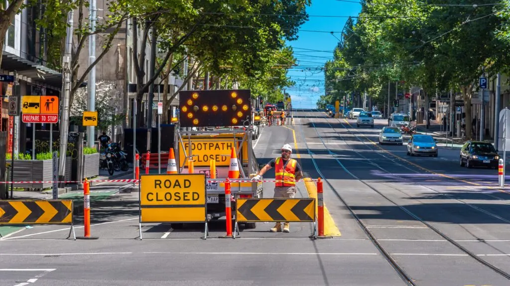 Traffic controller beside ROAD CLOSED and FOOTPATH CLOSED signs and cones on a closed city street