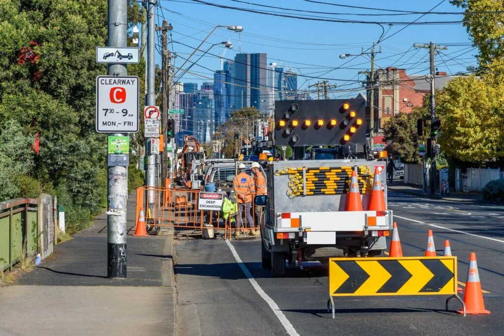 Traffic-control truck with arrow board and cones directing traffic past a roadside excavation