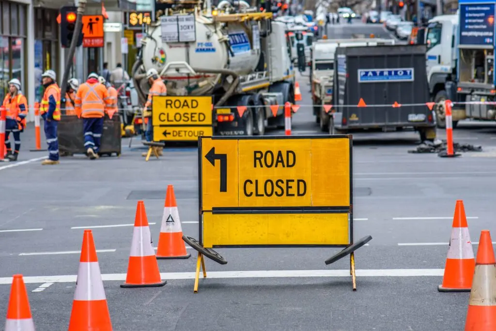 ROAD CLOSED detour sign and cones with workers and a truck at inner-city roadworks
